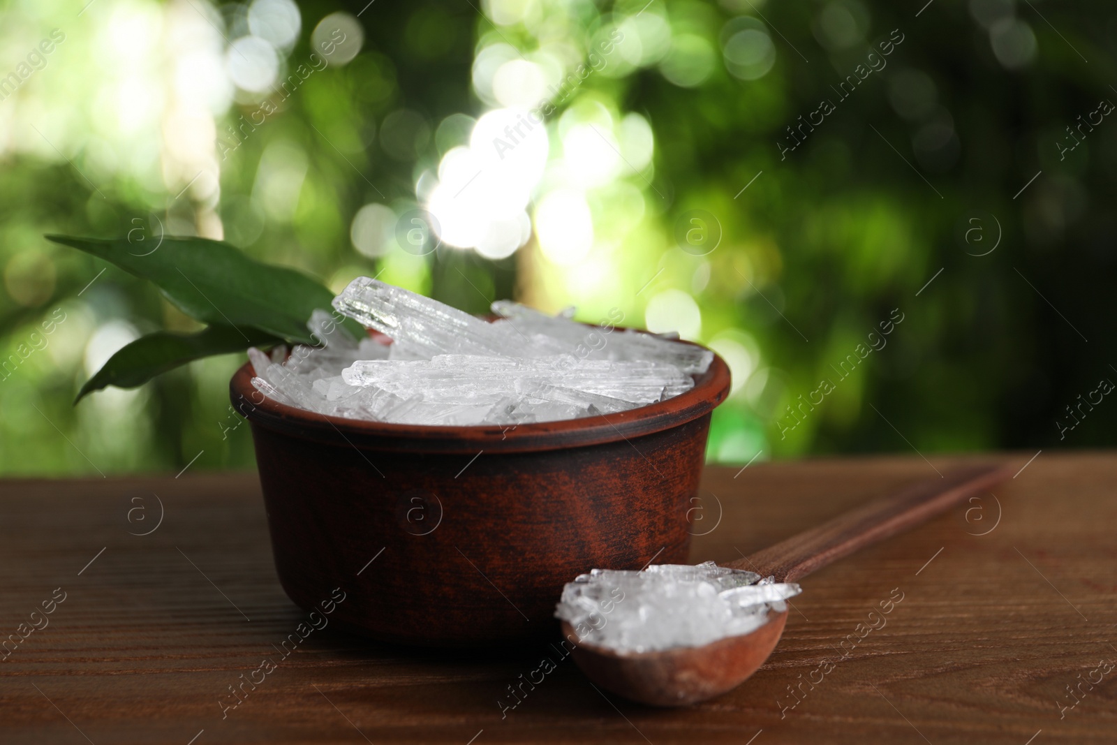 Photo of Bowl and spoon with menthol crystals on wooden table against blurred background