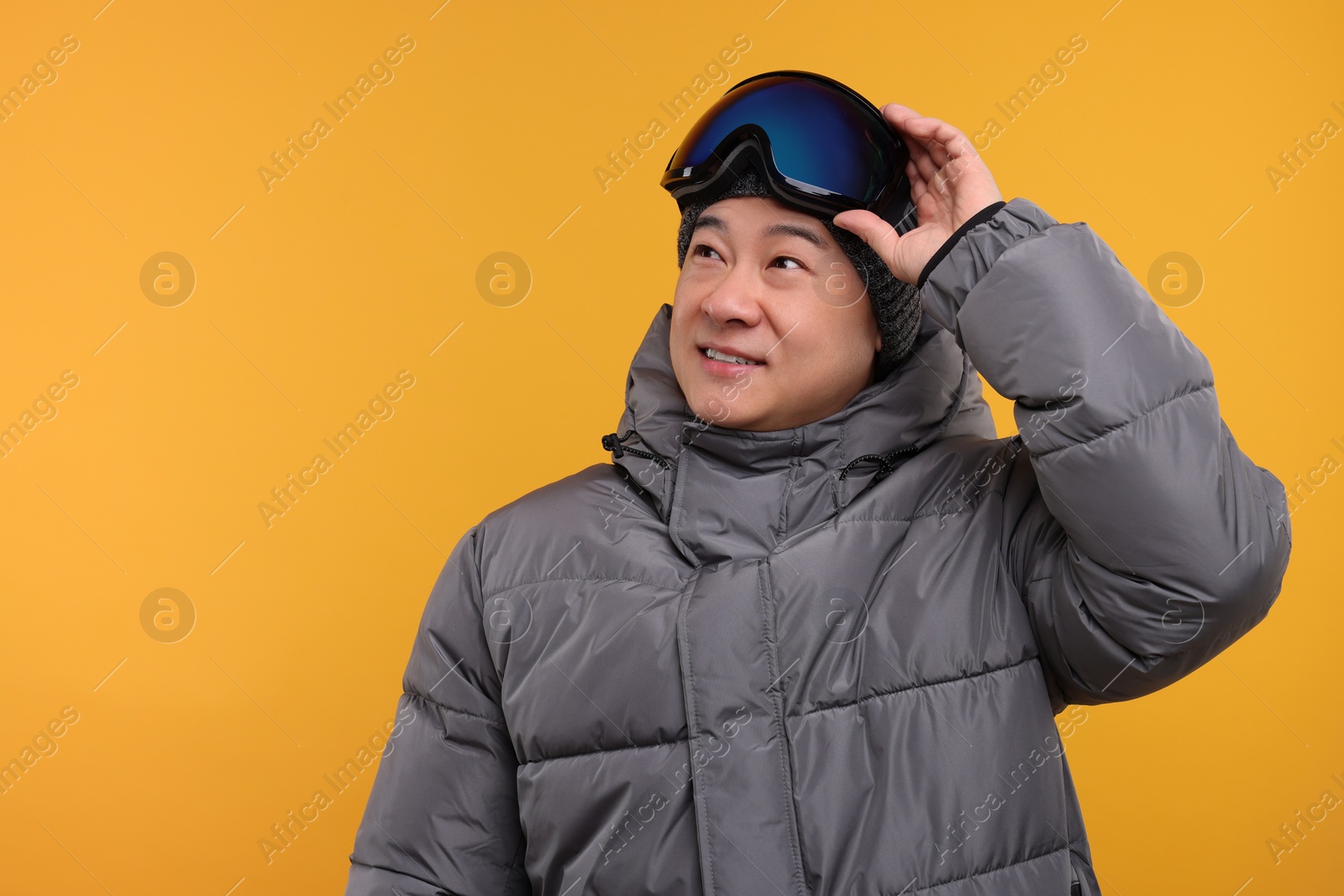 Photo of Winter sports. Happy man with ski goggles on orange background. Space for text