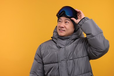 Winter sports. Happy man with ski goggles on orange background. Space for text