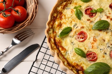 Photo of Delicious homemade cheese quiche, ingredients and cutlery on white wooden table, closeup