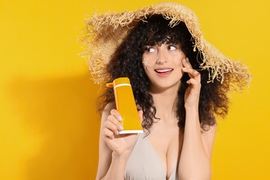 Photo of Beautiful happy woman in straw hat with sun protection cream on her face holding sunscreen against orange background