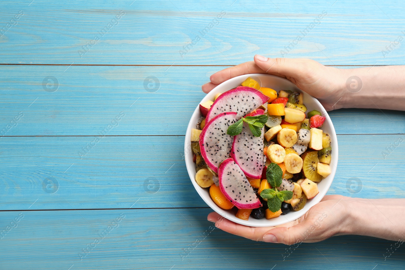 Photo of Woman with delicious exotic fruit salad at light blue wooden table, top view. Space for text