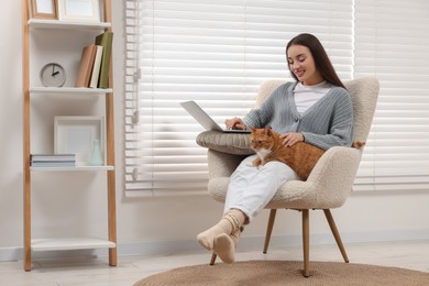 Photo of Happy woman working with laptop and petting cute cat at home