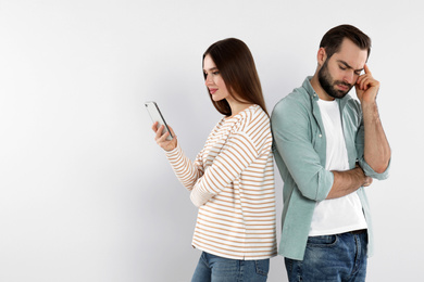 Photo of Woman with smartphone ignoring her boyfriend on light background. Relationship problems