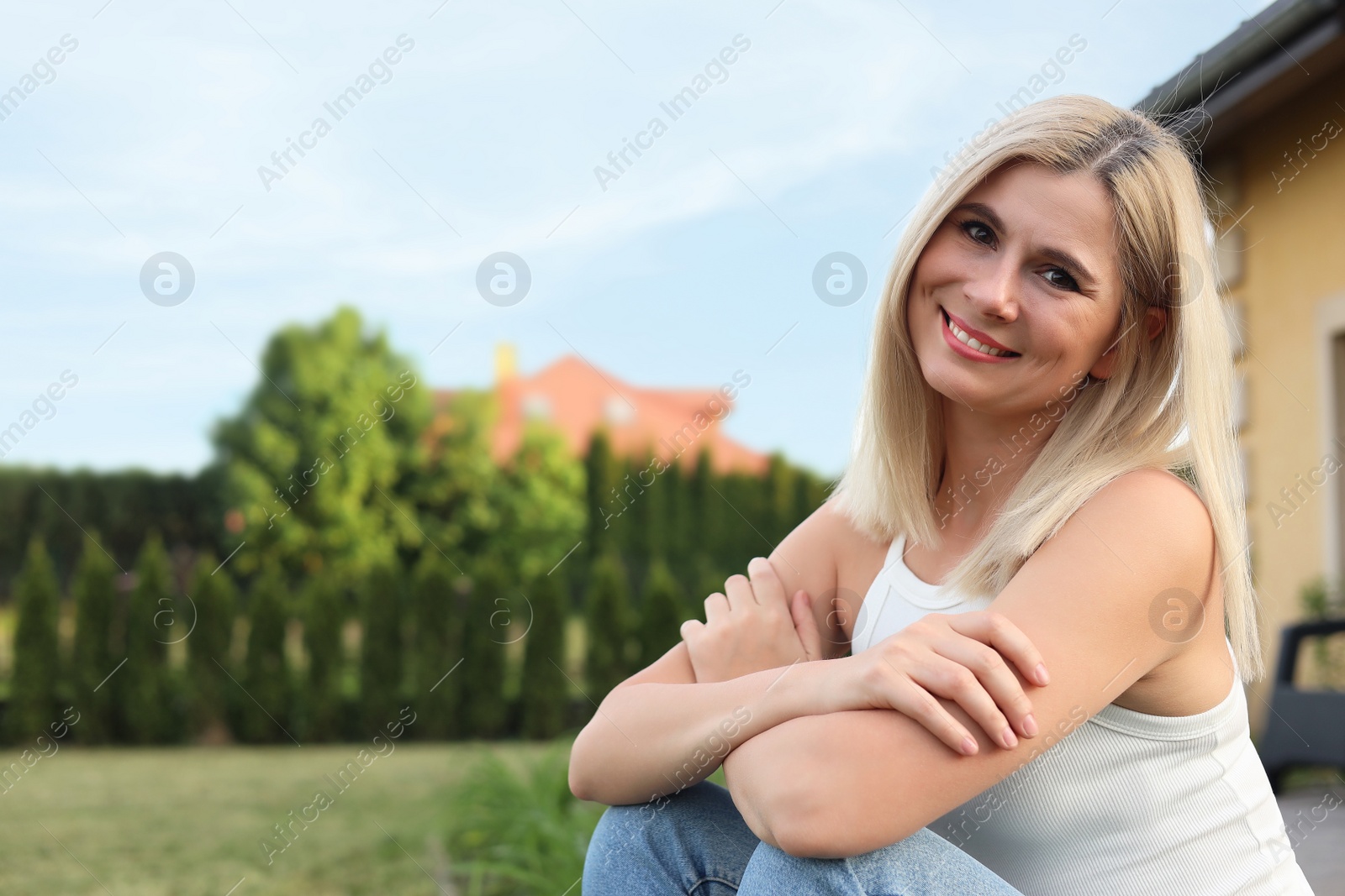 Photo of Portrait of beautiful woman sitting near house in yard, space for text