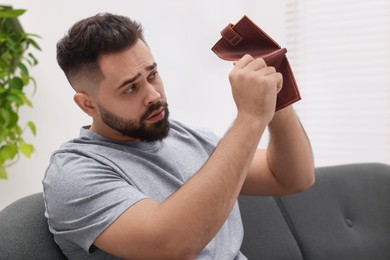 Photo of Upset man with empty wallet on sofa indoors