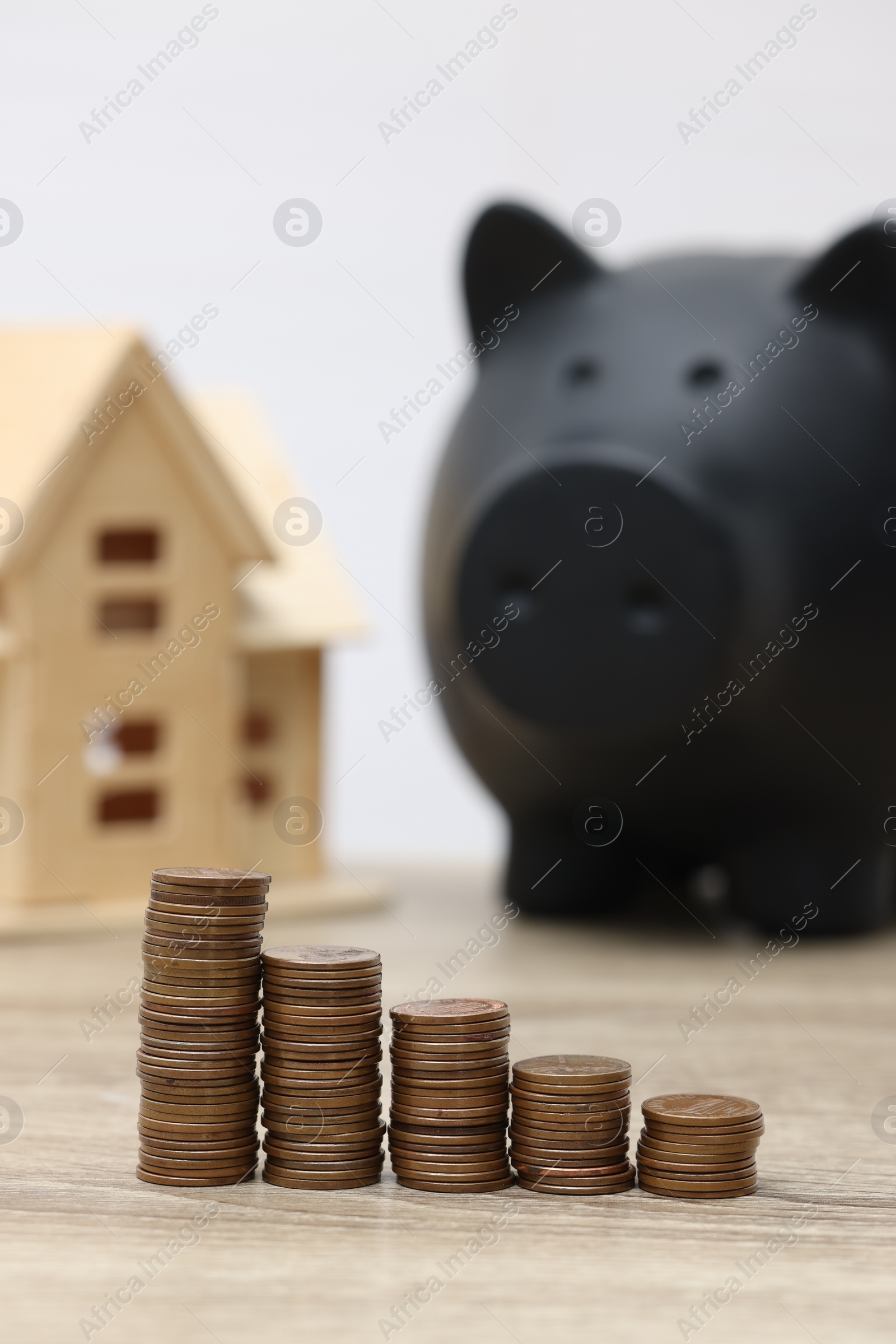 Photo of House model, piggy bank and stacked coins on wooden table, selective focus