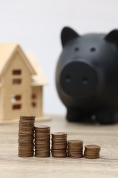 Photo of House model, piggy bank and stacked coins on wooden table, selective focus