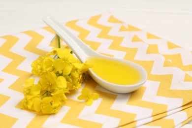 Rapeseed oil in gravy boat and beautiful yellow flowers on table, closeup
