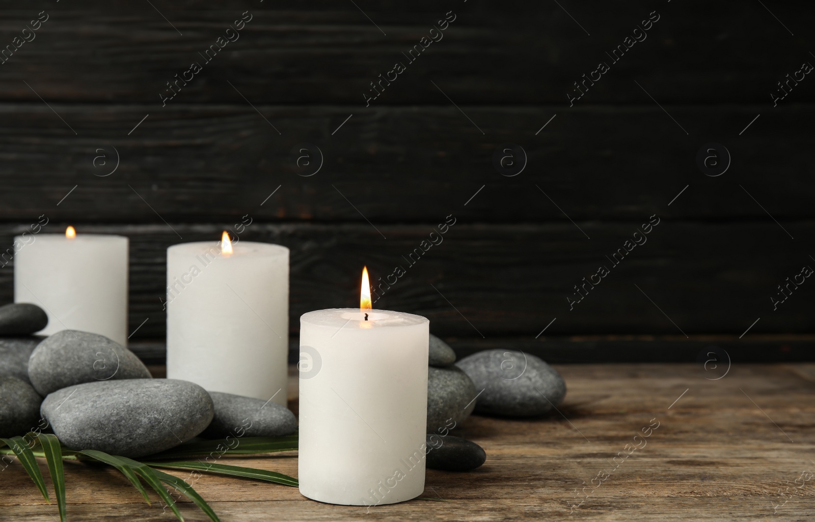 Photo of Burning candles, spa stones and palm leaf on wooden table, space for text