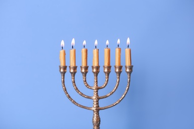 Photo of Golden menorah with burning candles on light blue background