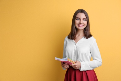 Portrait of female teacher with notebooks on color background