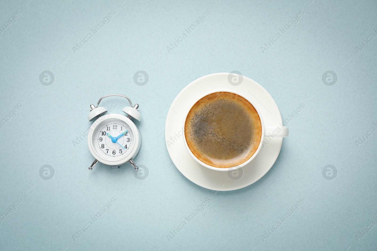 Photo of Cup of morning coffee and alarm clock on light background, flat lay