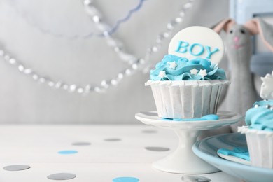Photo of Delicious cupcake with light blue cream and Boy topper on white wooden table, space for text. Baby shower party