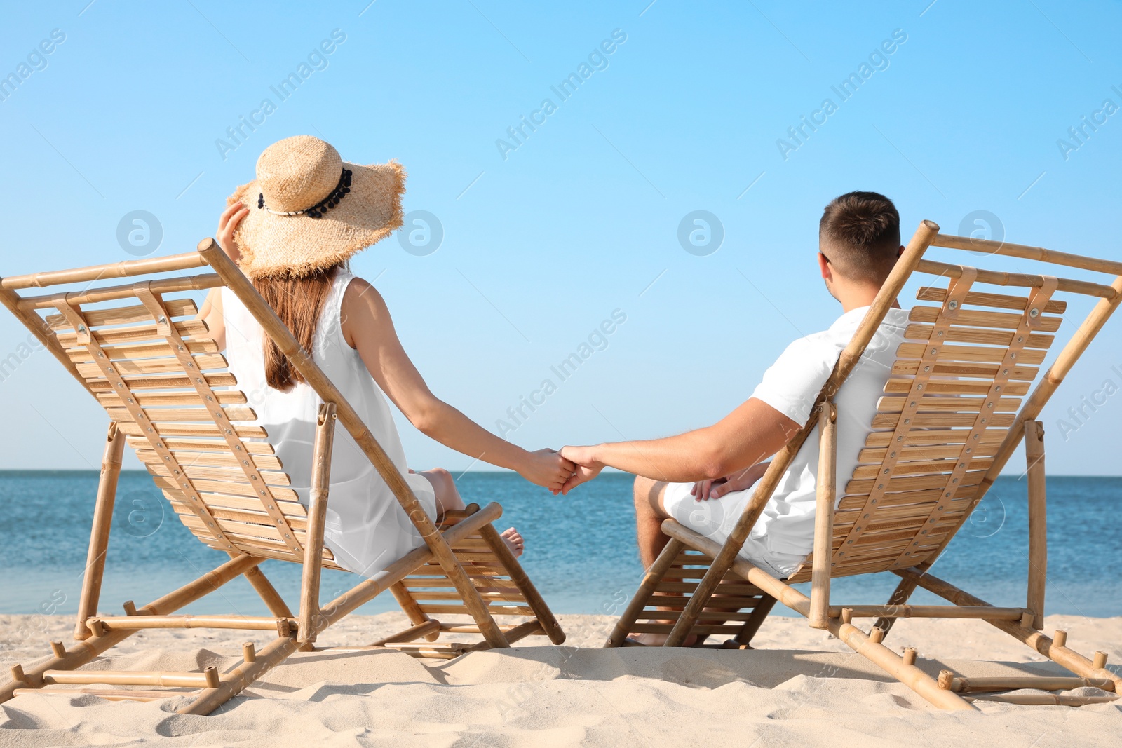 Photo of Young couple relaxing in deck chairs on beach