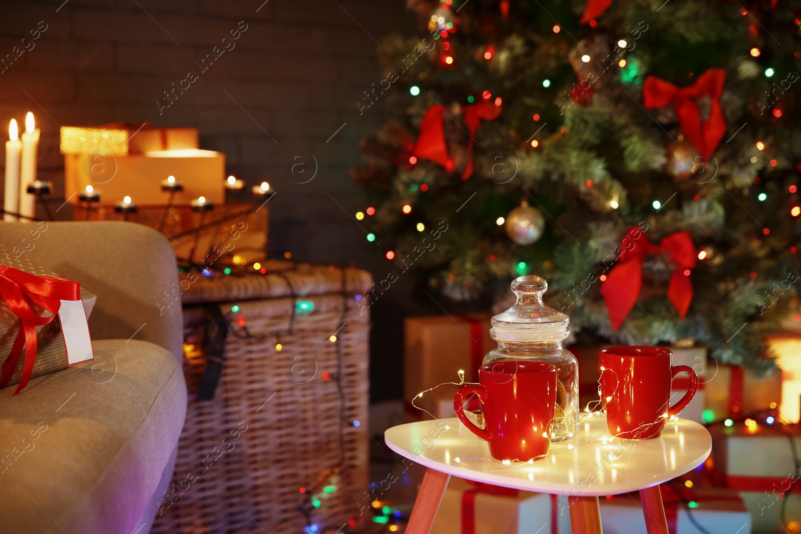 Photo of Cups and jar with cookies on table in room decorated for Christmas. Stylish interior