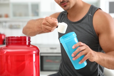 Young athletic man preparing protein shake in kitchen, closeup view