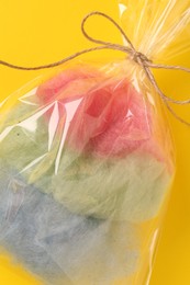 Photo of Packaged sweet cotton candy on yellow background, top view