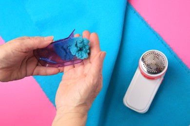 Photo of Woman emptying fabric shaver above light blue cloth on pink background, closeup