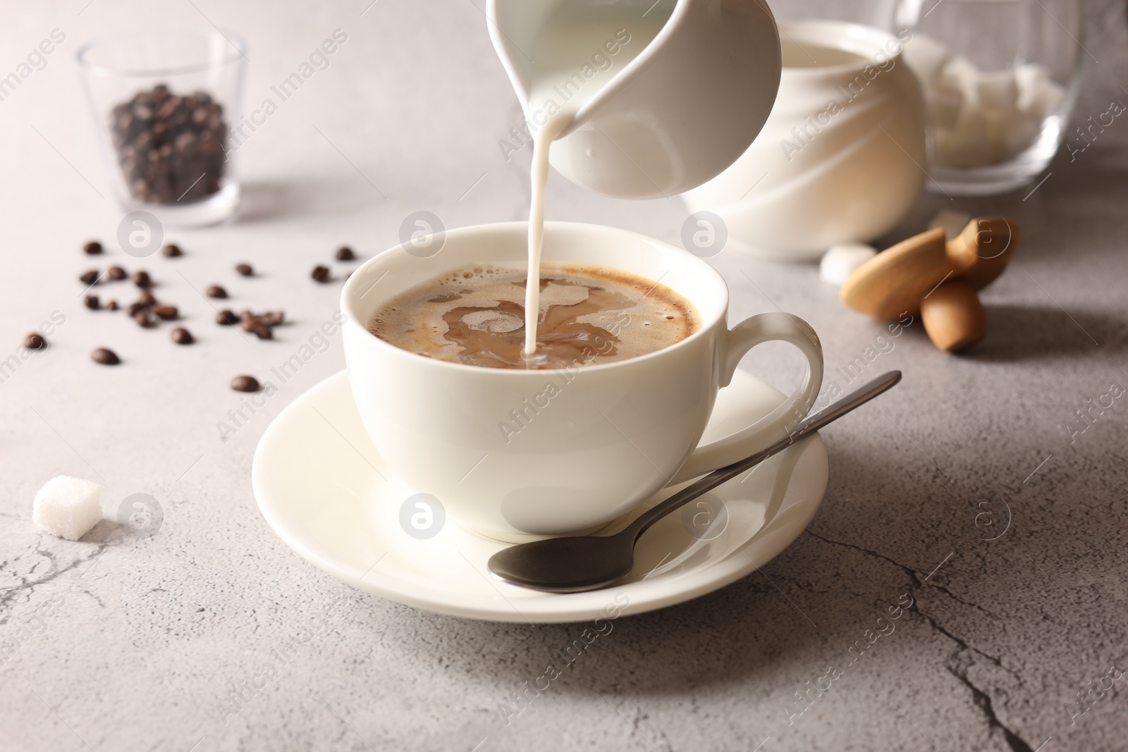 Photo of Pouring milk into cup with coffee on light grey textured table, closeup