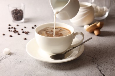 Pouring milk into cup with coffee on light grey textured table, closeup