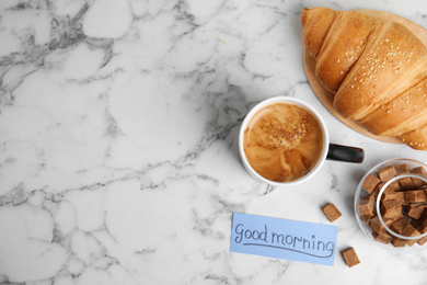 Photo of Delicious coffee, croissant and card with words GOOD MORNING on white marble table, flat lay. Space for text