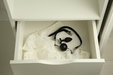 Photo of Anal plug, ball gag and women's underwear in open drawer of nightstand indoors, closeup. Sex toys