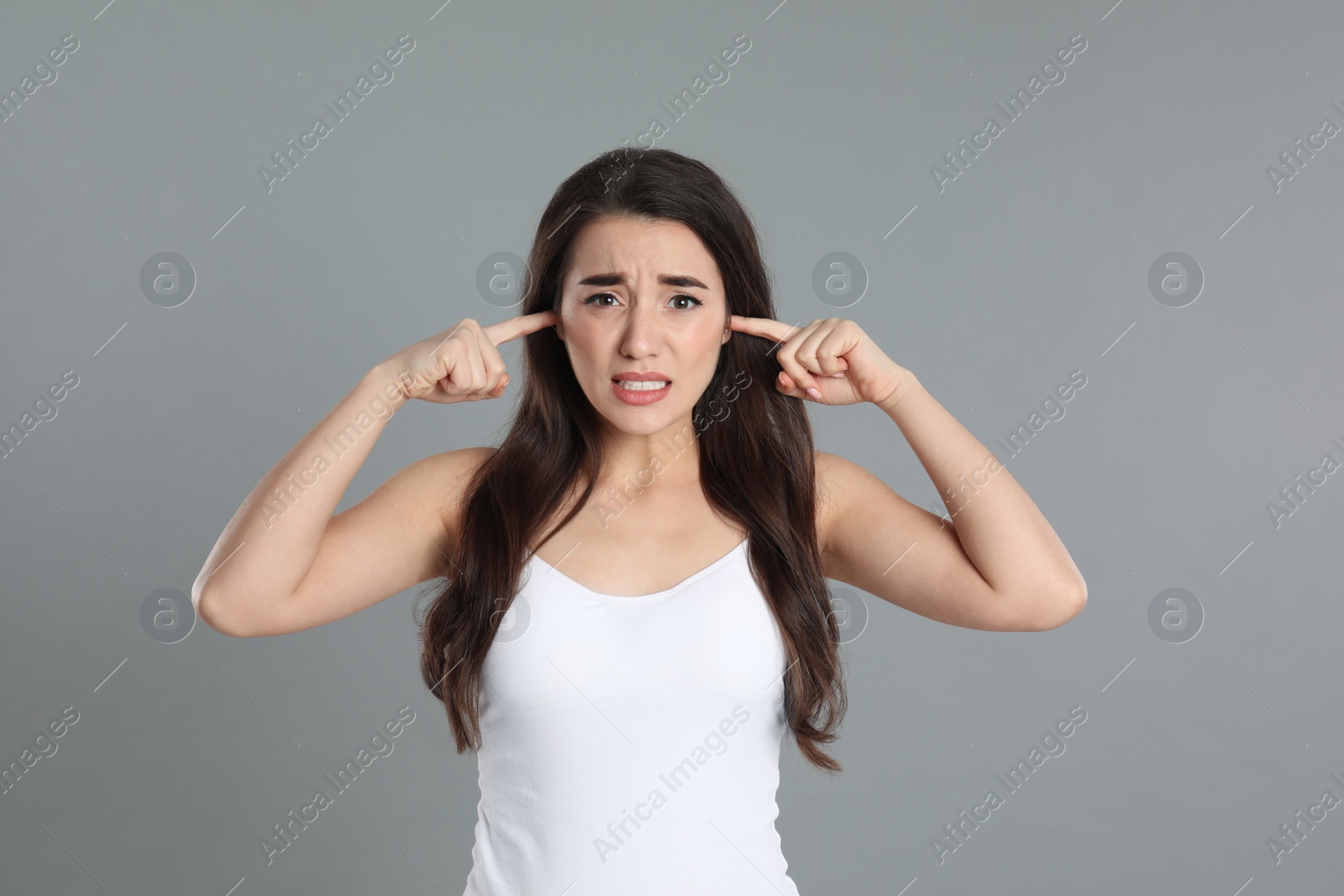 Photo of Emotional young woman covering ears with fingers on grey background