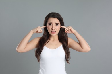 Photo of Emotional young woman covering ears with fingers on grey background