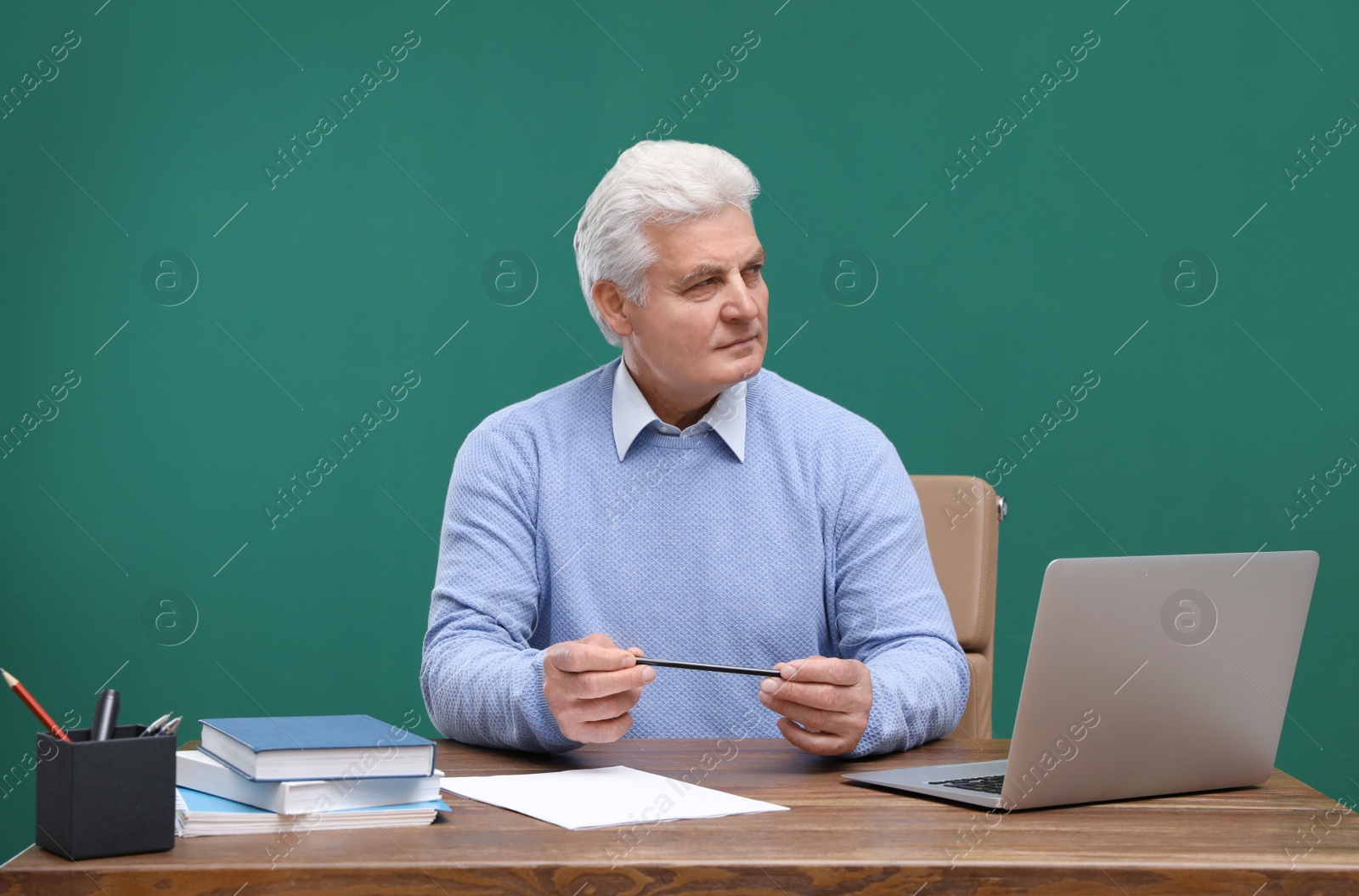 Photo of Portrait of senior teacher with laptop at table against green chalkboard