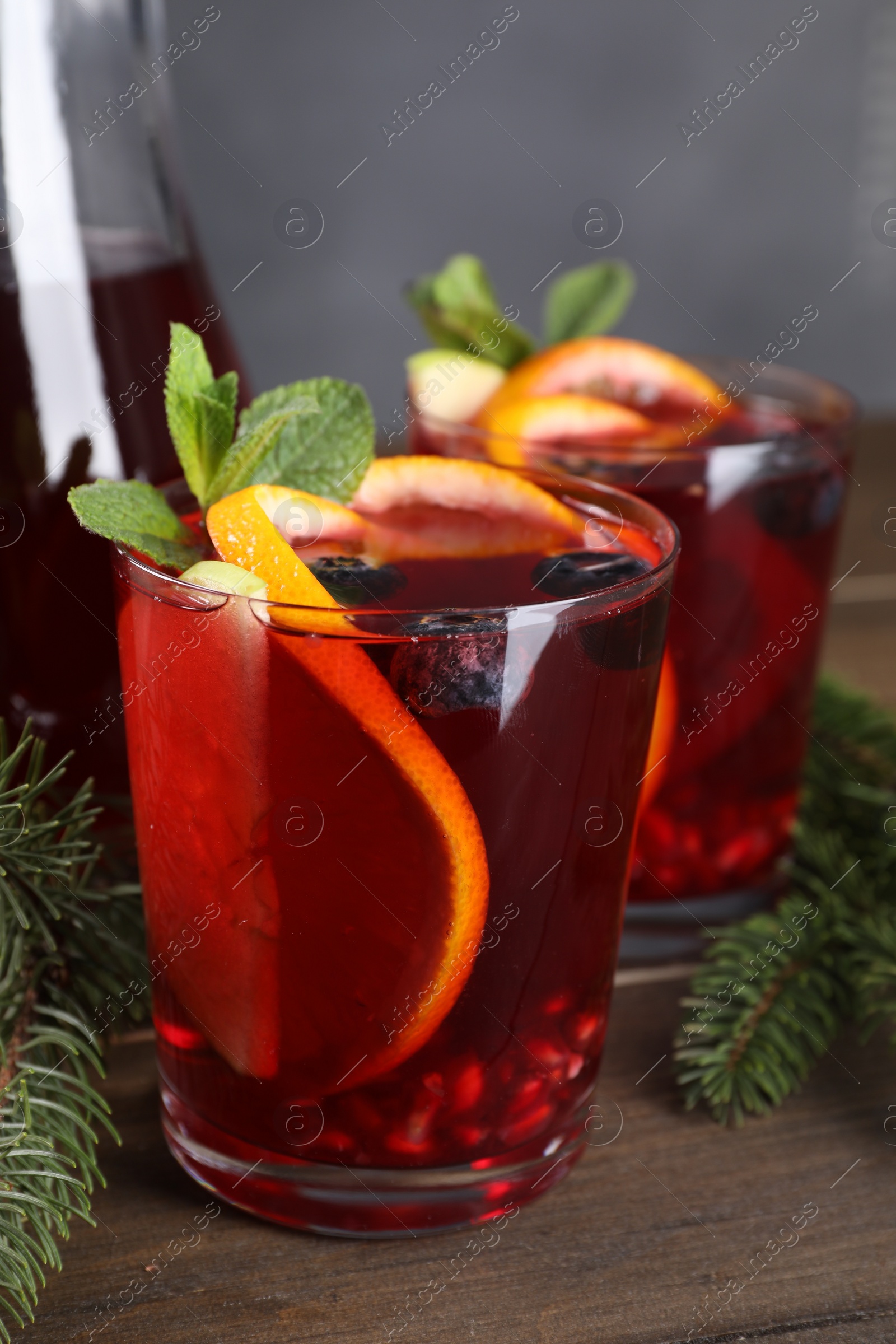 Photo of Aromatic Christmas Sangria drink and fir branches on wooden table, closeup