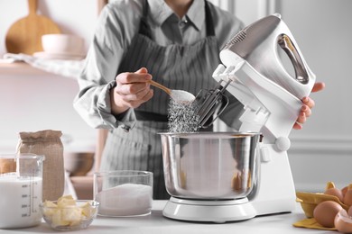 Photo of Woman adding sugar into bowl of stand mixer while making dough at table indoors, closeup