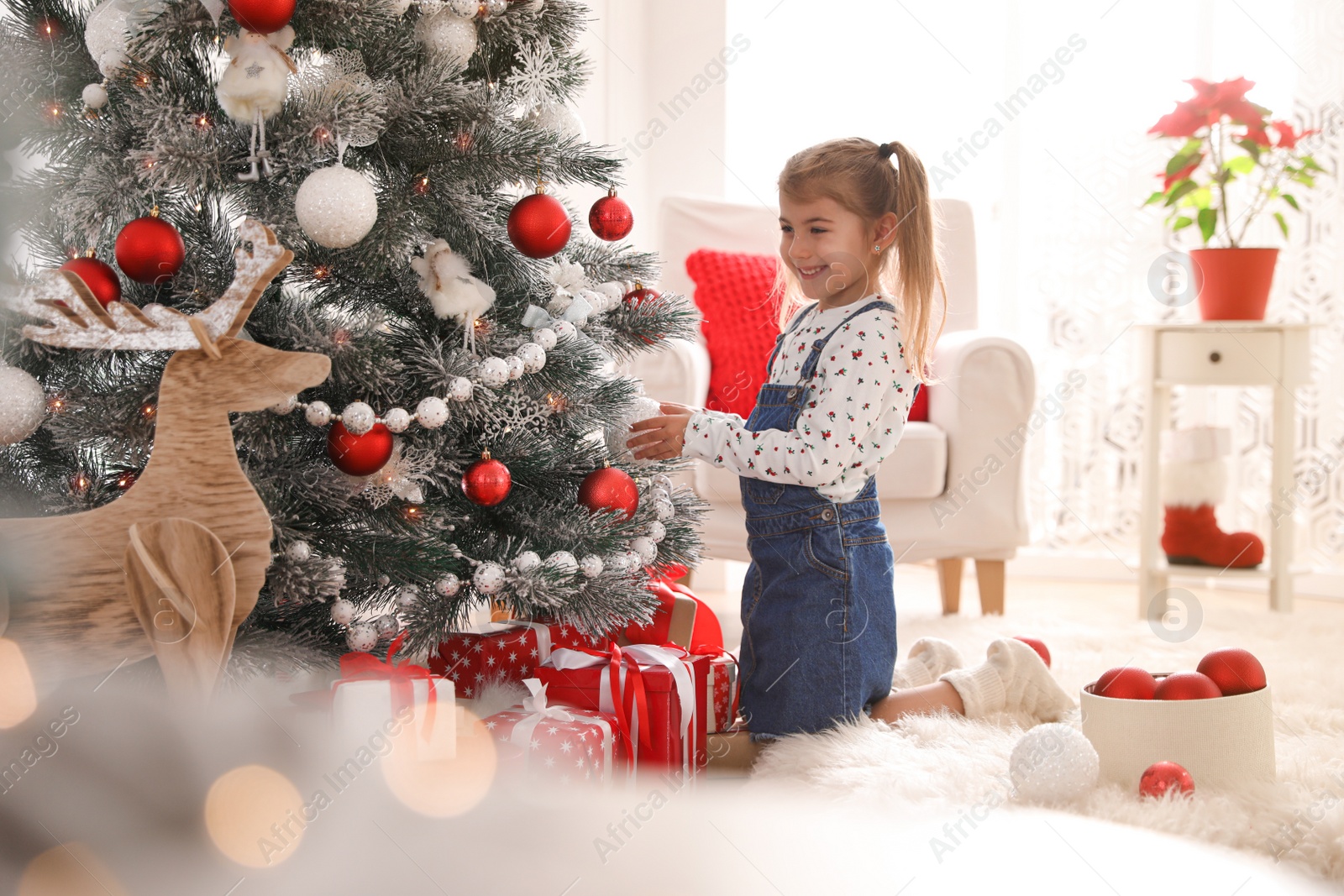 Photo of Cute little girl decorating Christmas tree at home