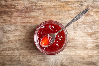 Photo of Jar and spoon with sweet jam on wooden background