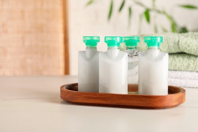 Mini bottles of cosmetic products on white table against blurred background. Space for text