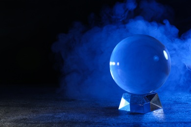 Photo of Magic crystal ball on table and smoke against dark background, space for text. Making predictions
