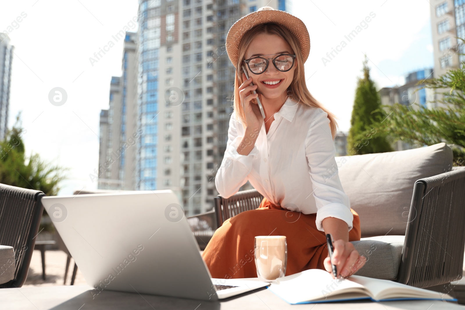 Photo of Beautiful woman with laptop talking on phone at outdoor cafe