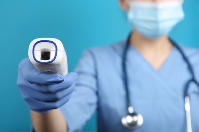 Photo of Doctor with infrared thermometer on blue background, closeup. Checking temperature during Covid-19 pandemic