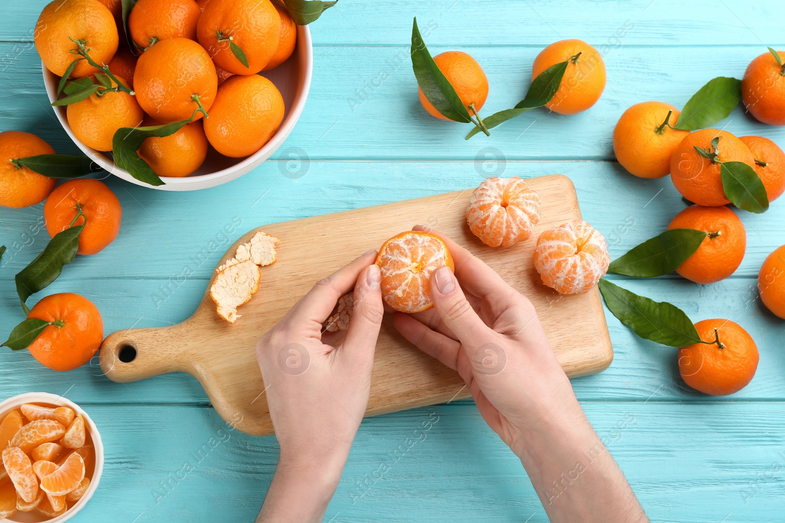 Photo of Woman peeling fresh ripe tangerine at light blue wooden table, top view