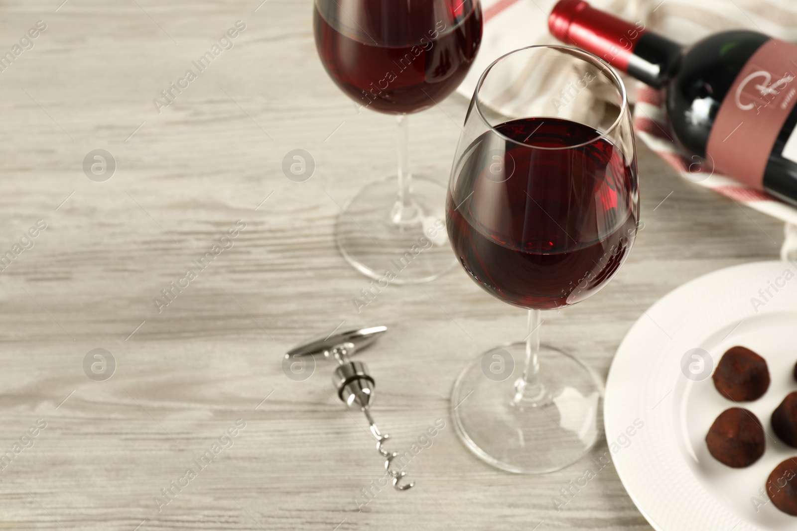 Photo of Glasses and bottle of red wine with chocolate candies on white wooden table. Space for text