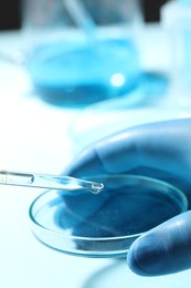 Photo of Doctor dripping liquid from pipette into petri dish in laboratory, closeup
