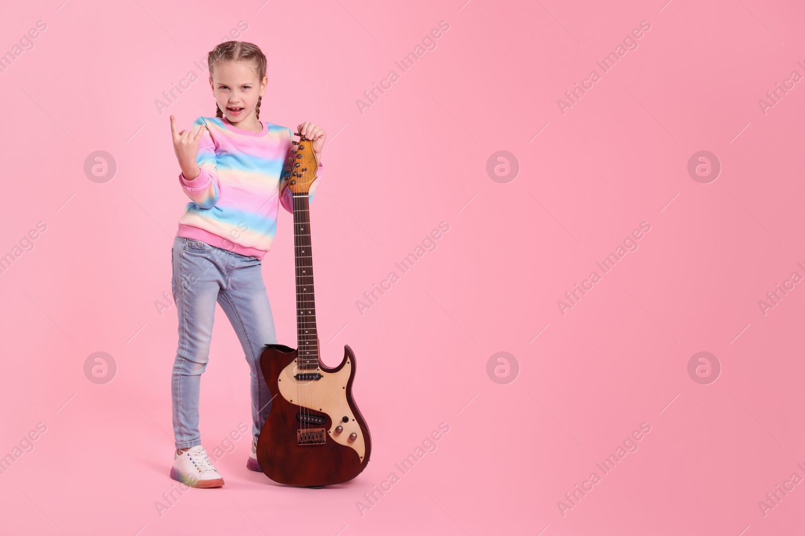 Photo of Cute girl with electric guitar on pink background. Space for text