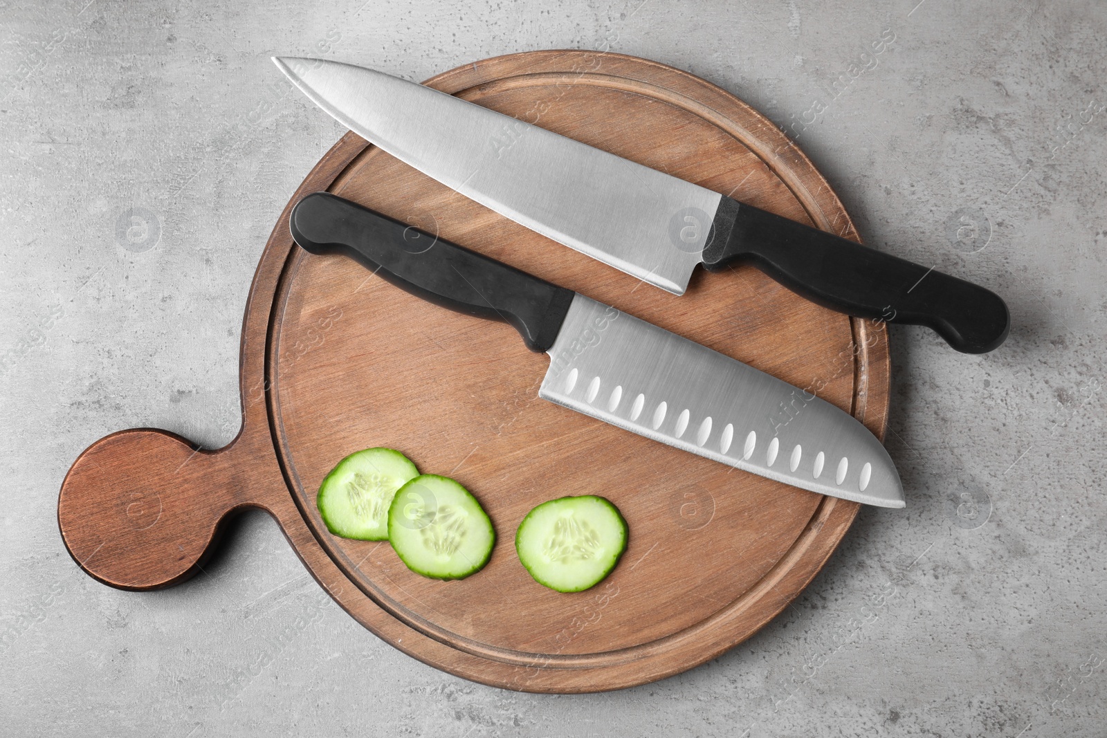 Photo of Wooden board with chef's knives and cut cucumber on grey background, top view