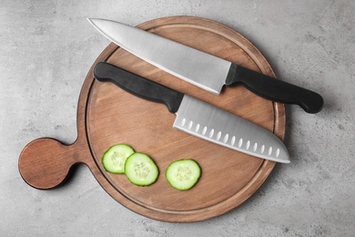 Wooden board with chef's knives and cut cucumber on grey background, top view