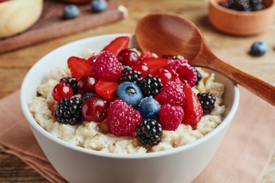 Photo of Bowl with tasty oatmeal porridge and berries served on wooden table, closeup. Healthy meal
