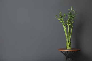 Vase with bamboo stems on table against grey wall, space for text