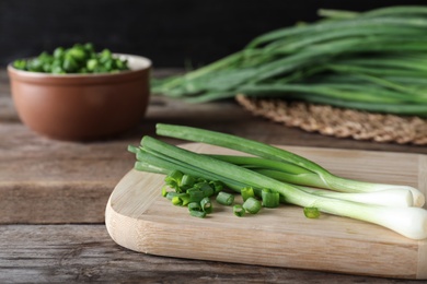 Photo of Wooden board with fresh green onions on table