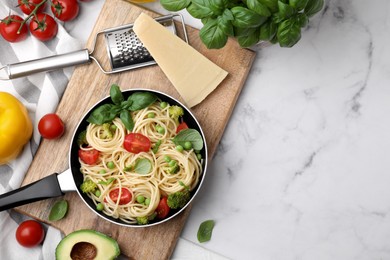 Photo of Delicious pasta primavera in frying pan and ingredients on white marble table, flat lay. Space for text