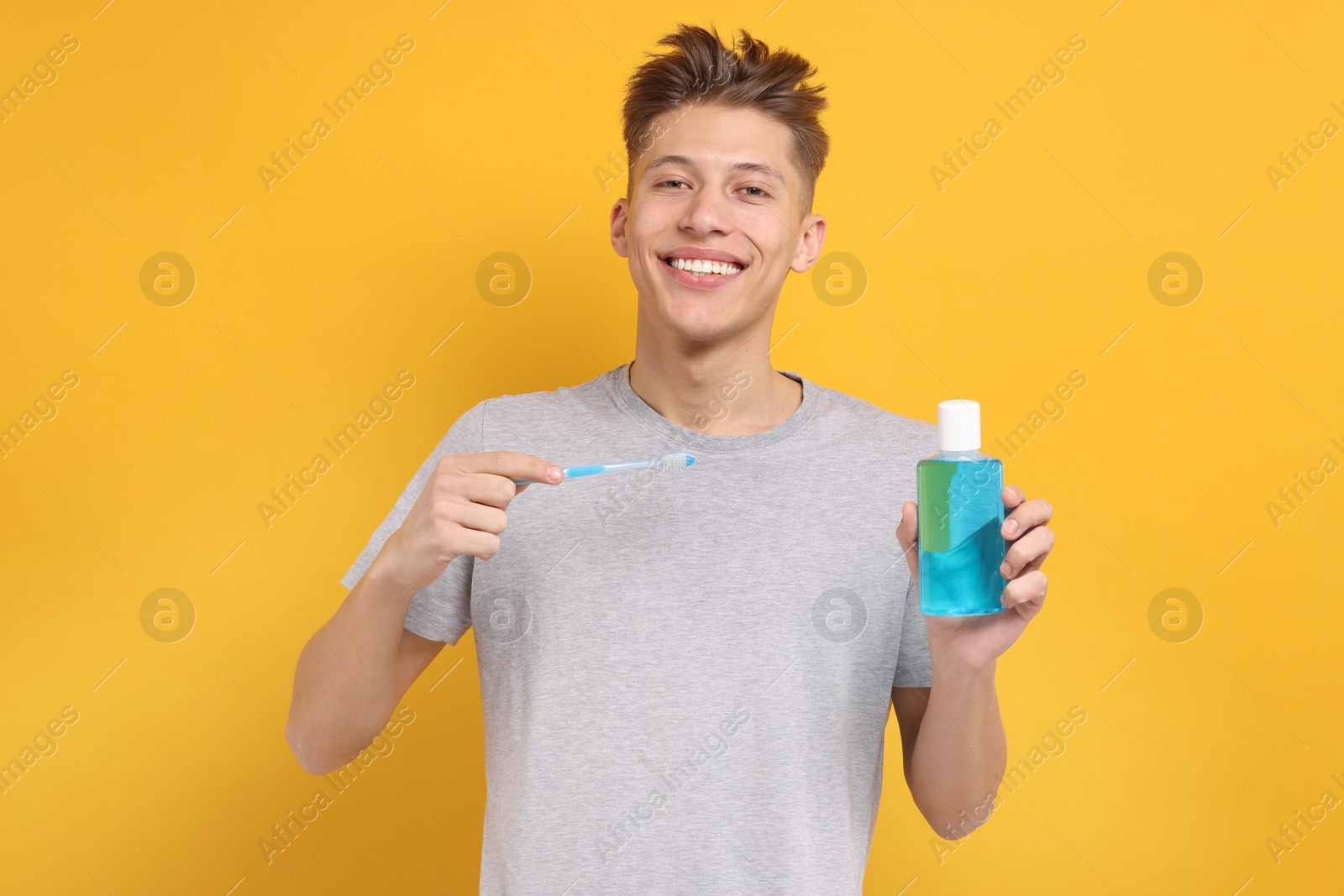 Photo of Young man with mouthwash and toothbrush on yellow background