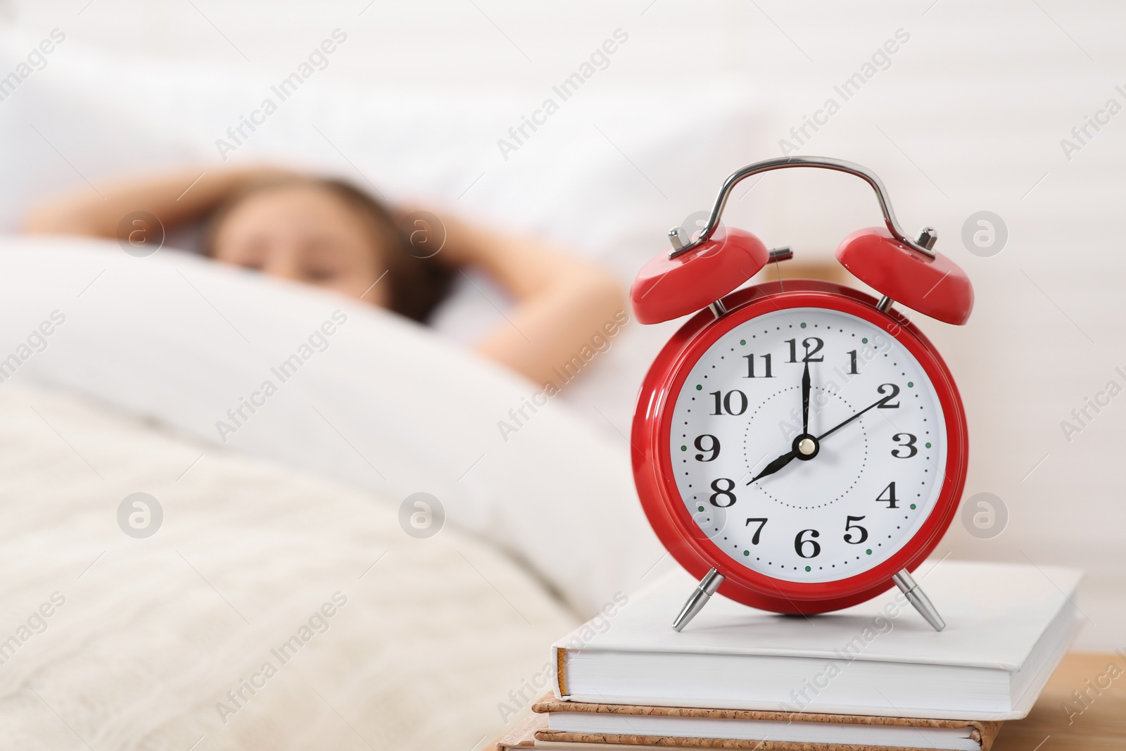 Photo of Cute little girl awaking in cosy bed, focus on alarm clock